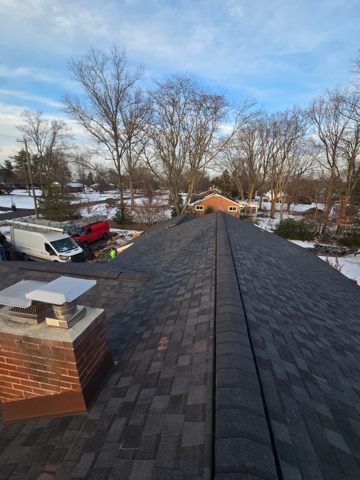 A finished dark grey shingle roof, photographed along the ridge past the brick chimney