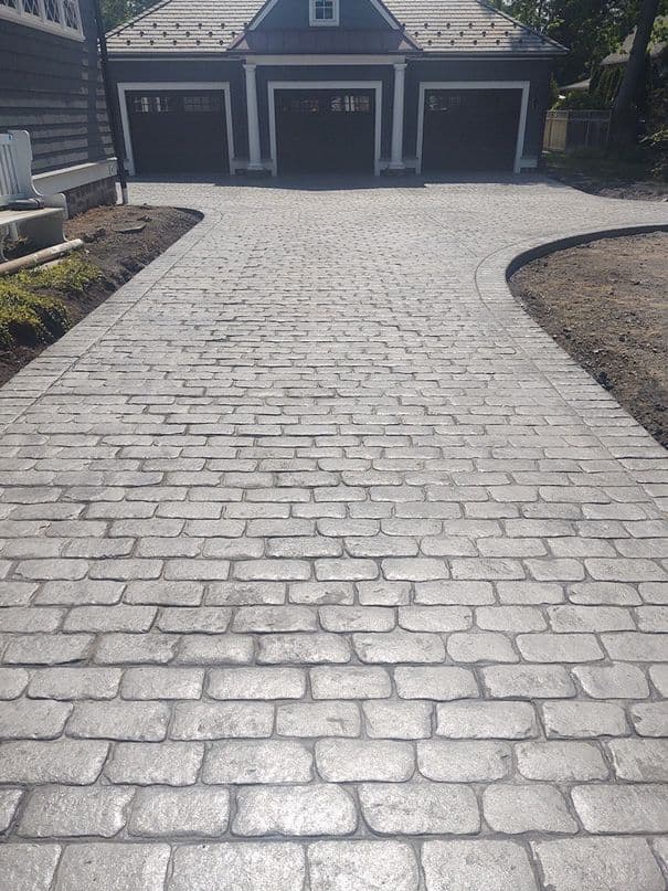 A pale stamped concrete driveway laid in a cobblestone pattern up to a garage