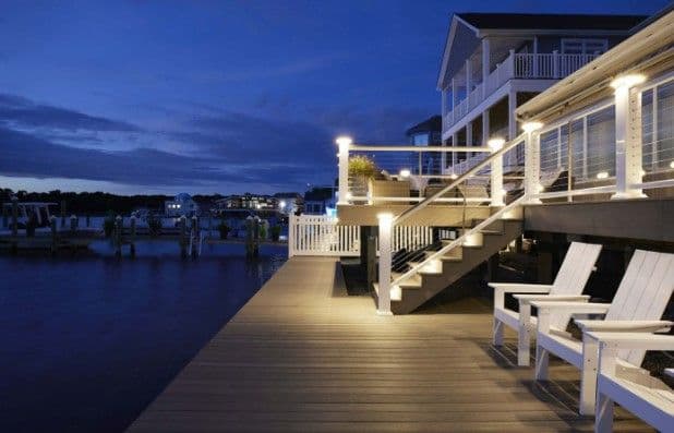A waterfront composite deck lit at dusk, with Adirondack chairs along the rail