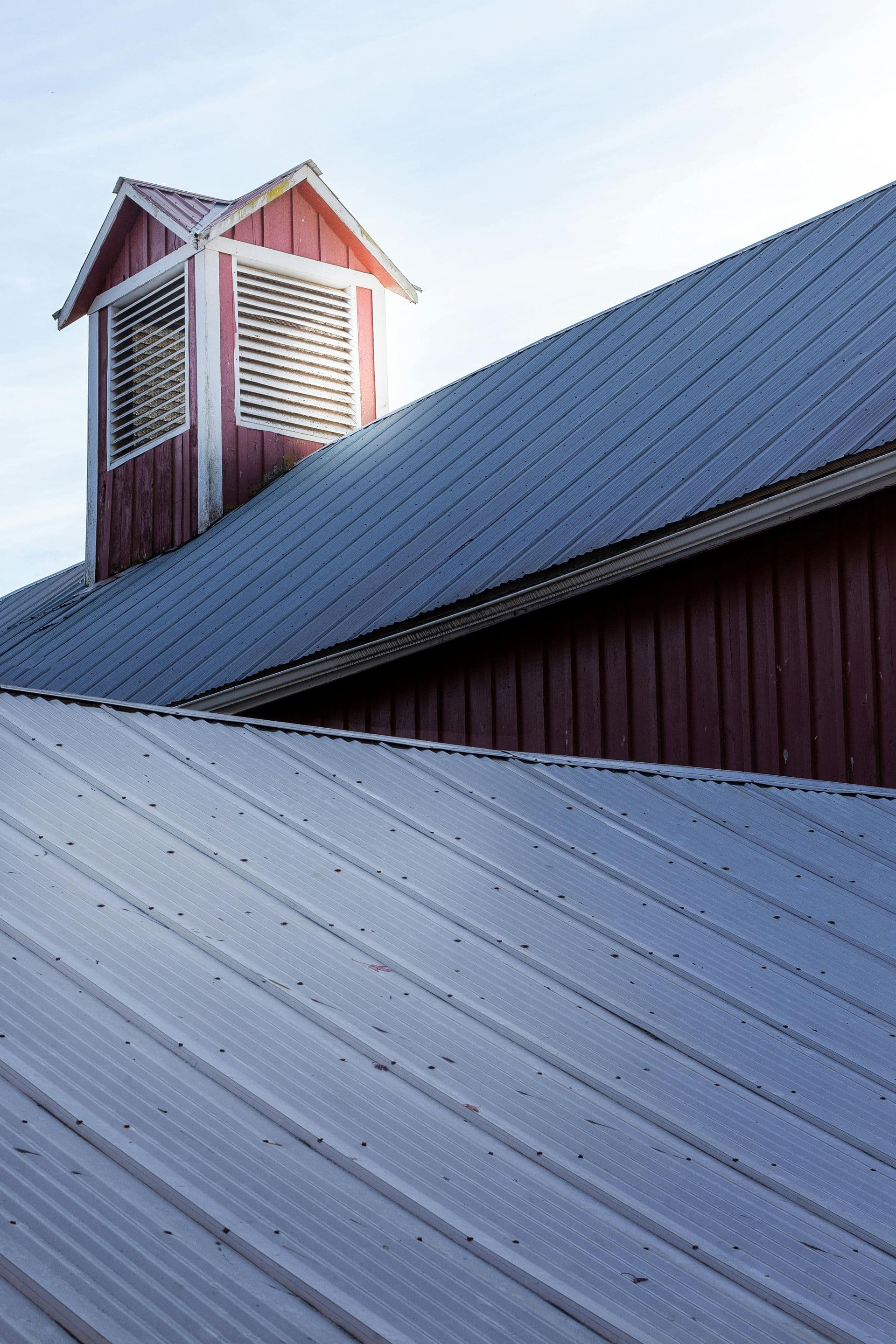 A dark standing-seam metal roof on a barn with a cupola