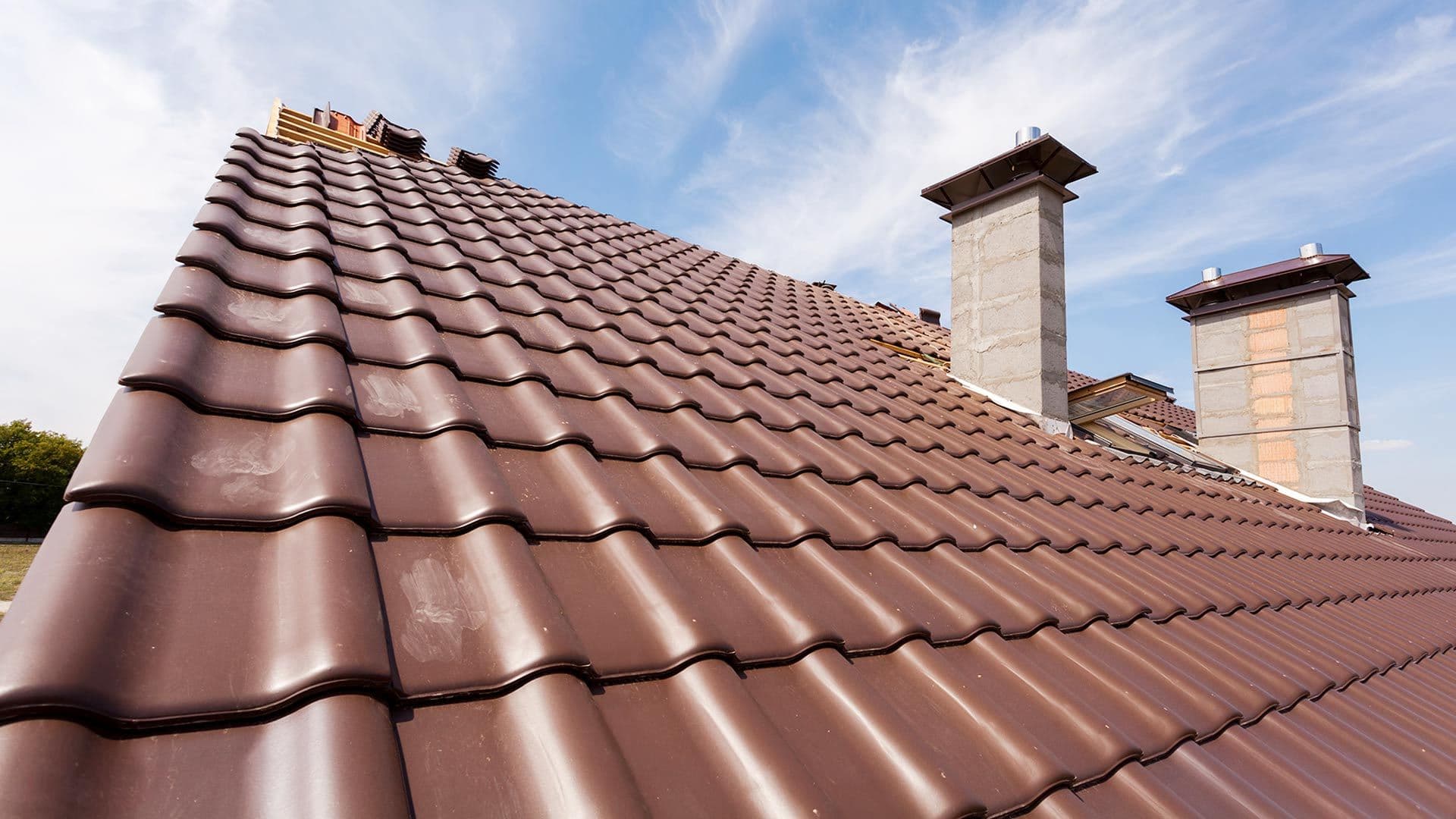 Close view of a terracotta tile roof running up to two chimneys