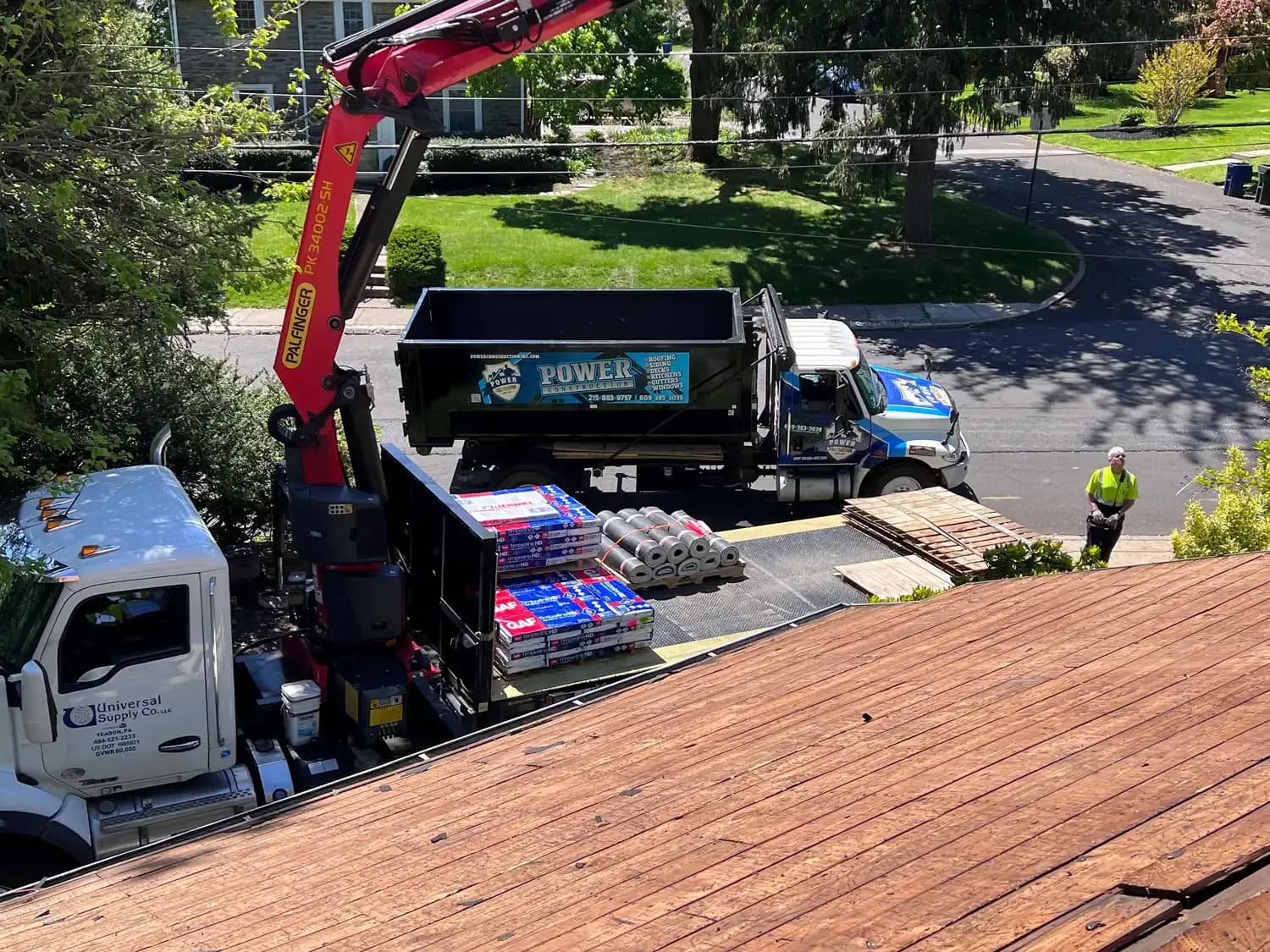 Aerial view of a Power Construction truck craning shingles up to a roof on a residential street